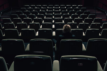 Fototapeta premium Alone in a dark empty theater, a person sits surrounded by rows of cinema seats.