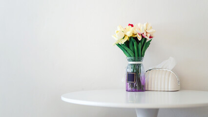 Simple and elegant bouquet in glass vase on round white table against plain wall, ideal for minimalist interior decor.