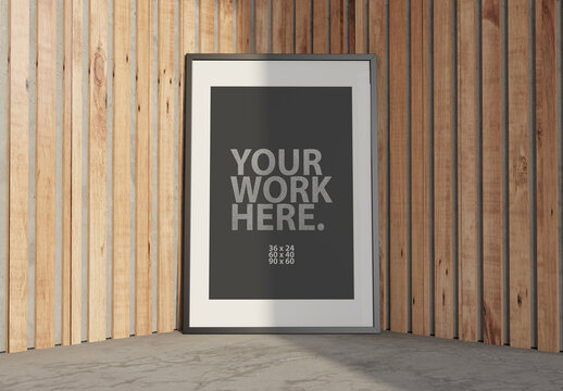 Vertical Poster with Black Frame Mockup standing on the floor next to wooden wall