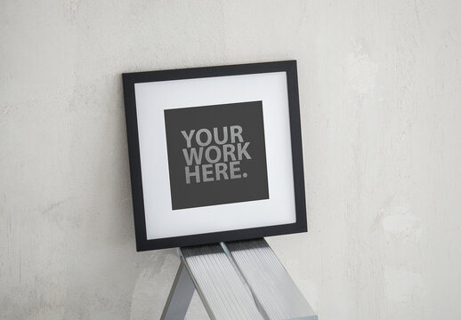 Square poster black frame mockup with passepartout standing on a ladder