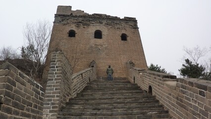 Abandoned tower on the Great Wall of China with steps leading up to it.  white sky in the background.