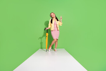 Full body portrait of pretty young woman wear jacket dress walk podium show v-sign isolated on green color background