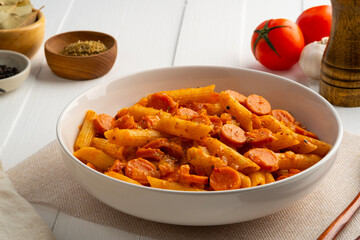 Sausage pasta,Stir fried penne rigate pasta with tomato sauce and cheddar cheese in white plate.