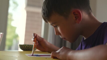 Young boy painting inivations with crosses on them to first communion - side profile