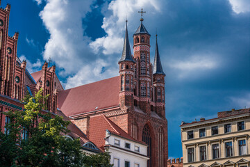 Fototapeta premium Scenic view of the historic Old Town in Toruń, Poland, featuring charming medieval buildings and the impressive silhouette of a Gothic church in the background.