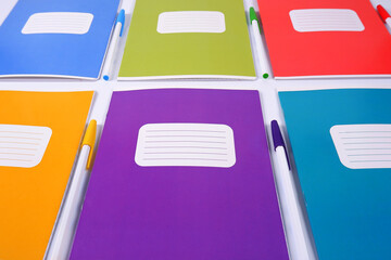 Colorful school notebooks lie in a row with pens highlighted on a white background.Purchase, sale of school supplies, stationery store.An empty template for the logo.Back to school.