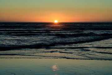 The sunset on the horizon is reflected on the sandy beach