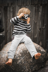A little boy with a camera in his hands against the background of a wooden wall © Marcin