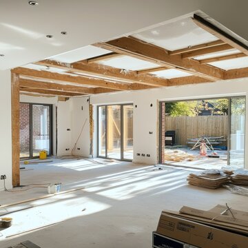 The interior of a modern home extension under renovation, with exposed beams and natural light flooding in