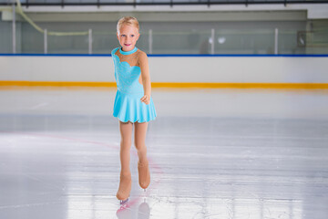 Full length portrait of little girl doing figure skating on indoor rink during performance
