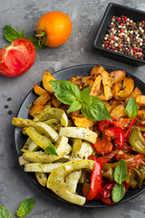 Plate with healthy, baked, vegetable salad of potatoes, zucchini, sweet peppers with herbs on a dark background. Dietary nutrition, healthy lifestyle, vegetarianism.