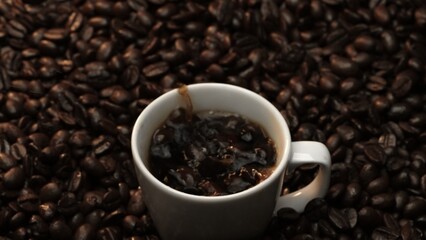 Close up of coffee bean drop in to hot espresso with pile of coffee seed. Macro of freshly roasted bean falling in to cup with aromatic smoke. Slow motion. Organic coffee seed concept. Comestible.