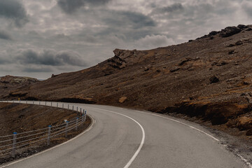 A winding road cuts through Iceland's rugged volcanic landscape under a dramatic sky