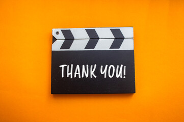 Thank you message written on movie clapper board with orange background. Conceptual thank you...