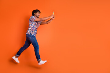 Full body photo of attractive young man hold device running dressed stylish colorful clothes isolated on orange color background