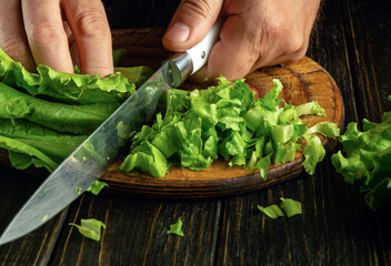Cutting lettuce leaves with a knife in the hand of a chef. Service concept in the hotel and restaurant business.