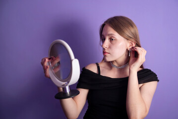 Young beautiful teenage girl tries on new silver earrings with stones and looks in mirror, the girl is going on her first date and thinks what to wear