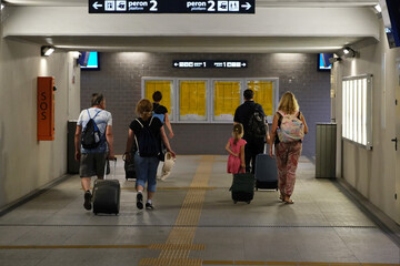 Fototapeta premium People with wheeled suitcases are walking in station tunnel to catch train