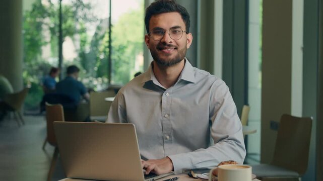 Indian Arabian man businessman ethnic guy business freelancer entrepreneur distant work computer laptop online studying male customer visitor order food coffee in cafe restaurant happy cheerful smile