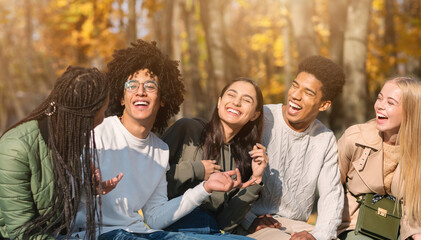 Obraz premium Multiracial teenagers having fun at public park, sitting on bench and talking, copy space