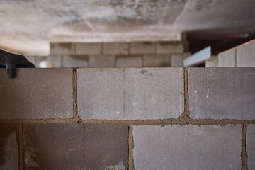 A construction worker is expertly laying cinder blocks within the ongoing building project
