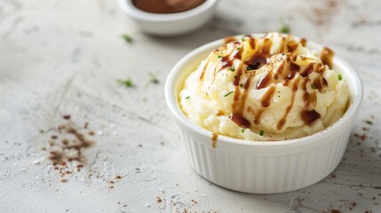 Mashed Potatoes with brown sauce in a white cup on a table with empty space in the background