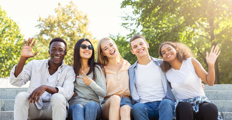Happy friends international students spending time together in the summer city, sitting on stairs...