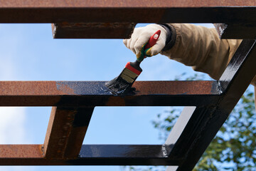 A man applying anti-corrosion primer to a metal structure. Fragment of a man's hand with a molar...