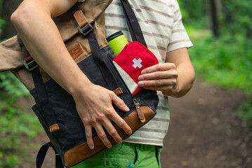 Close-up of a person taking a first aid kit out of a backpack while on a forest trail, highlighting...