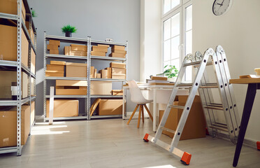 Interior of empty work space with office desk in warehouse with shelves filled cardboard boxes of retail products. Business workplace used for shipping merchandise and stock inventory.