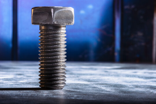 Close up of a single metal bolt on a metallic surface with dark tonned background