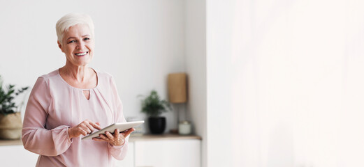Cheerful beautiful senior woman using digital tablet at home, empty space