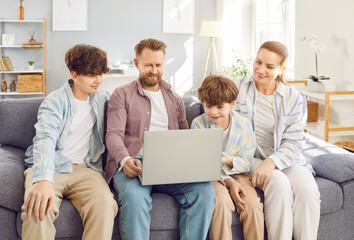 Obraz premium Happy family with teen and little kid sons sitting on sofa to have fun using modern new laptop together, smiling parents rest on couch to enjoy weekend with children, watch video on computer at home