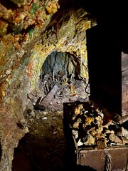 A dimly lit mine tunnel filled with rusty equipment and a cart loaded with ore, highlighting the gritty reality of underground work. A captivating glimpse into the industrial past.
