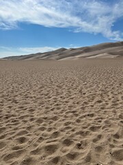 A vast expanse of sand stretches under a clear blue sky, with gentle dunes rising in the distance. This serene and minimalist landscape is ideal for themes of solitude, nature, and tranquility. 