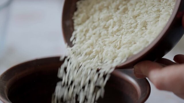 Women's hands pour white rice from one bowl to another. Cooking in the home kitchen.