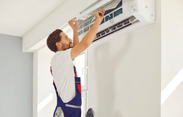 Portrait of professional electrician man with screwdriver maintaining, cleaning modern air conditioner indoors. Young male technician repairing or installing air conditioner at home or at office.