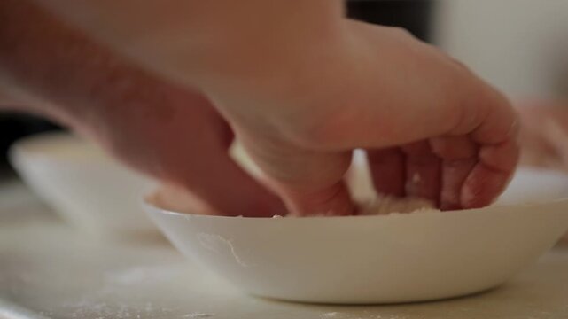 The process of cooking homemade chicken wiener schnitzel. The woman dips the beaten meat in flour, and then in beaten eggs and puts it on the stove to fry.