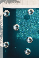 Top view of silver disco balls floating in a crystal-clear pool under sunlight in summer in tropical destination