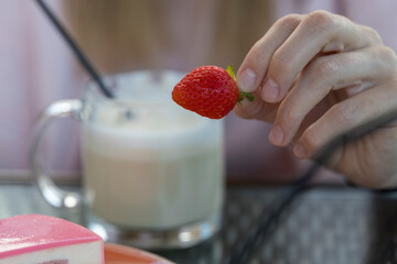 A person is holding a strawberry in front of a cup of coffee