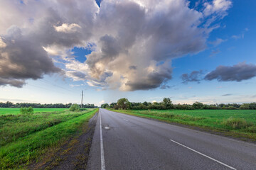 A road with a few trees in the background and a few birds flying in the sky