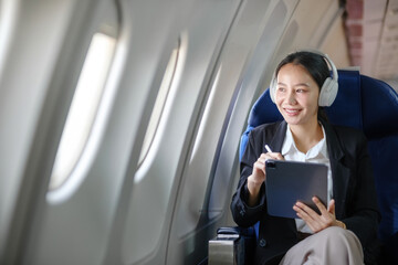 A woman is sitting in an airplane with a tablet and headphones on