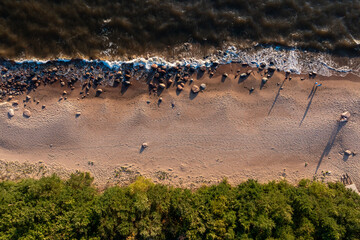 The shore of a beach with waves washing up on the sandy coast, rocks scattered along the water's...