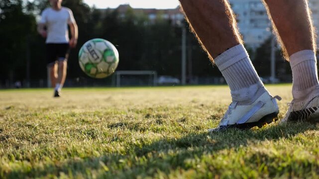 Male feet of professional footballers passing soccer ball on stadium at sunset. Legs of sportsmen kicking ball at green field. Young men training at meadow. Concept of a freestyle football. Slow mo