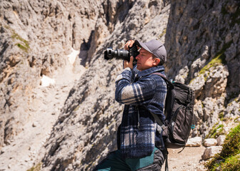 Male photographer takes a picture with a professional camera during a hike in  Dolomite Alps, South Tyrol, Italy 