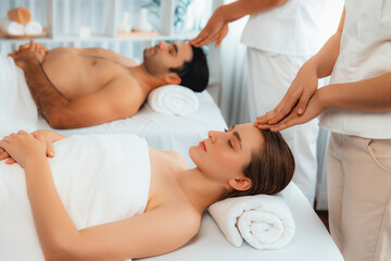 Caucasian couple enjoying relaxing anti-stress head massage and pampering facial beauty skin recreation leisure in dayspa modern light ambient at luxury resort or hotel spa salon. Quiescent