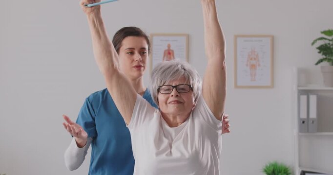 Senior woman exercising with nurse, using fitness rubber band, health care of elderly people, young female geriatric nurse helping old woman with bending side, doctor caring for physical well-being