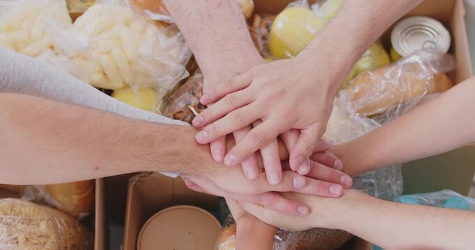 Top view of team of volunteers putting their hands in stack working in charitable foundation finishing packing donations box. Volunteering, humanitarian aid concept. 4k video. Slow motion video.