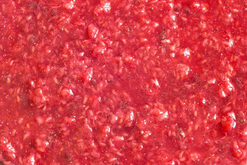 This vibrant close-up image showcases the rich texture of crushed natural raspberries. The mix of red and pink hues highlights the freshness of the fruit, with visible seeds adding to the organic feel