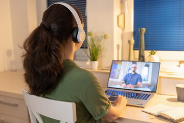 Back view of young woman working at laptop and wearing headphones. Freelance and online education....